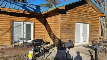 Eine Blockhütte mit zwei Türen, einer Terrasse mit Gartenmöbeln und einem Grill.