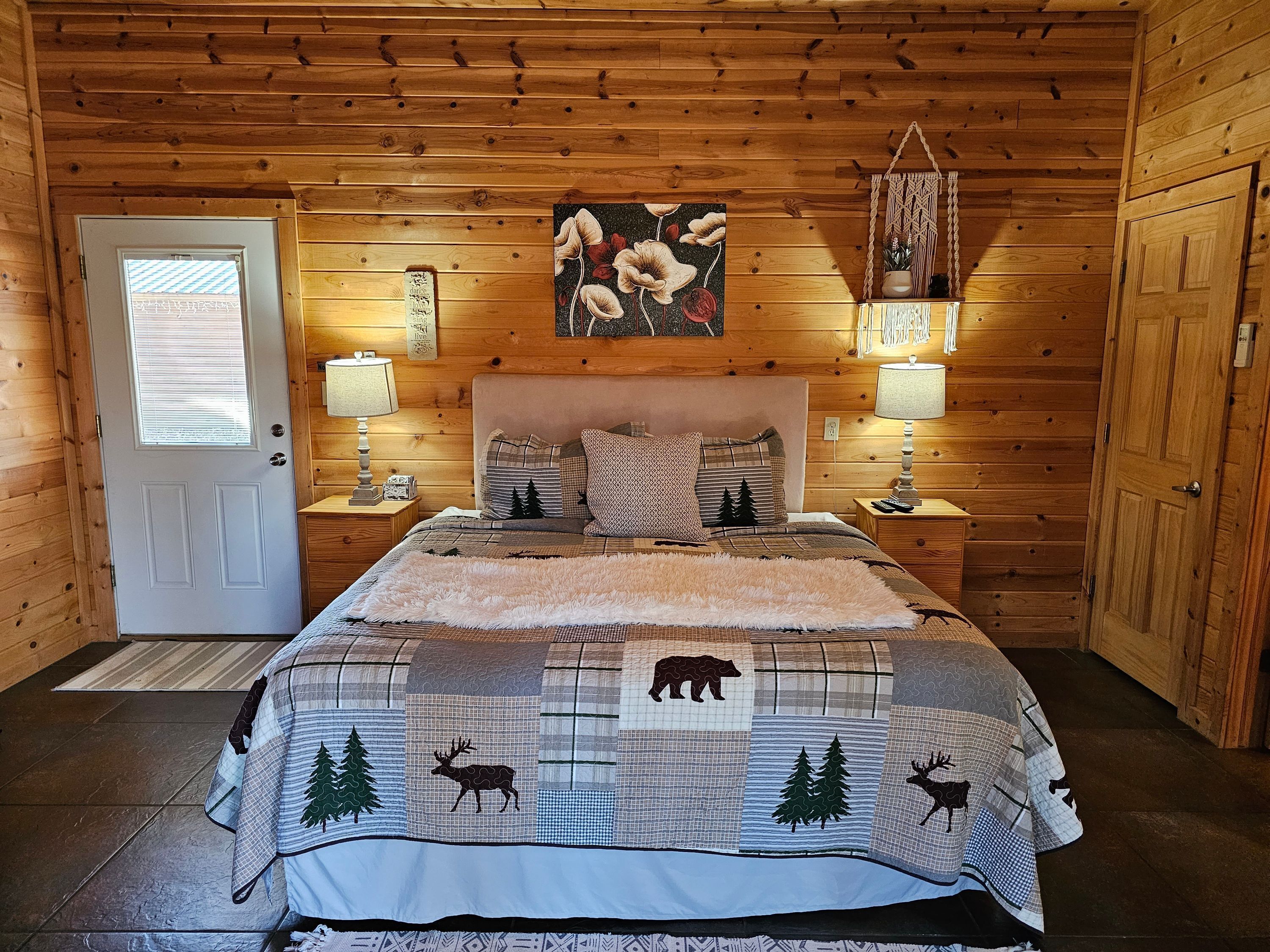 A wooden cabin bedroom with a bed, two bedside tables, a door, and a wall-mounted painting.
