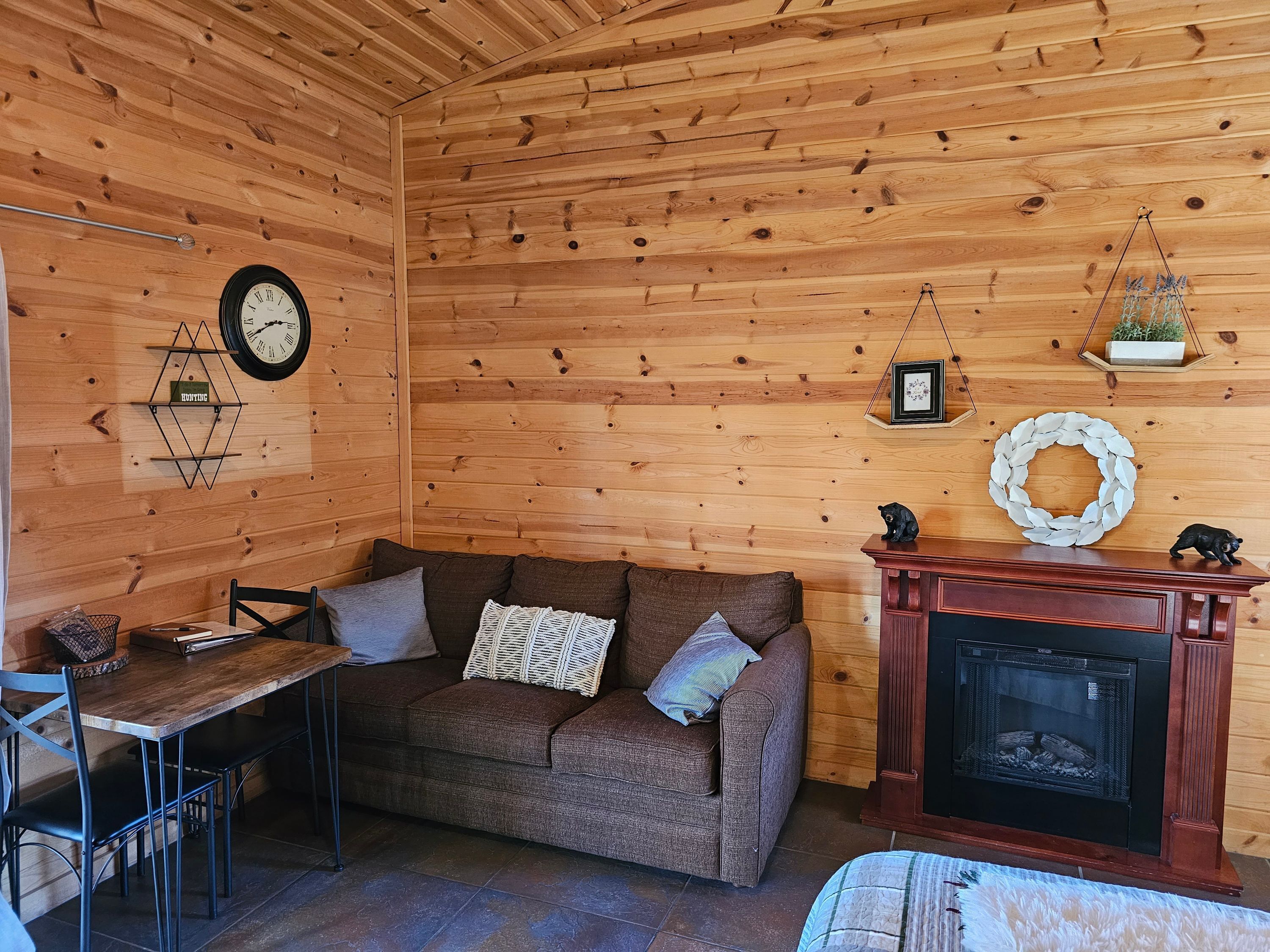 L’intérieur chaleureux d’un chalet avec un mur en bois, un canapé, une table à manger, une cheminée et une horloge.