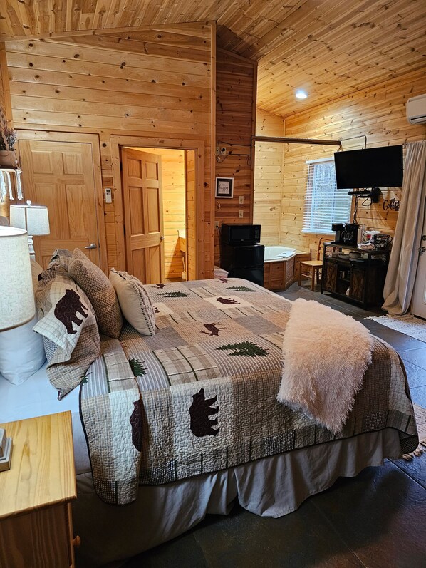 Acogedora habitación tipo cabaña de madera con cama, escritorio, silla, televisor y una estación para café.