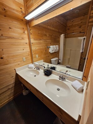 Baño de cabaña de madera con dos lavamanos, un espejo y una ducha.