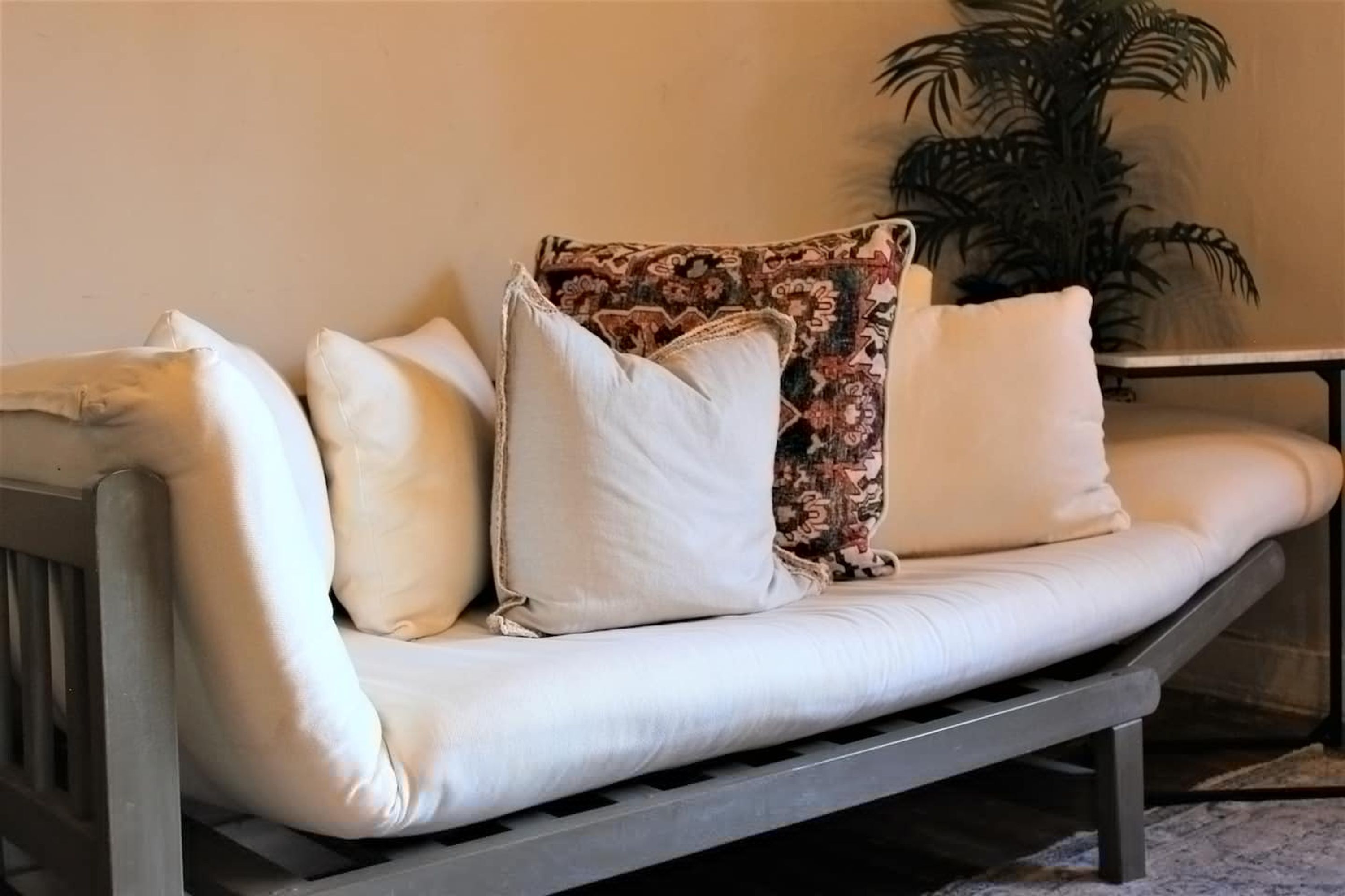 A sofa with multiple cushions, a patterned throw, and a potted plant in the background.