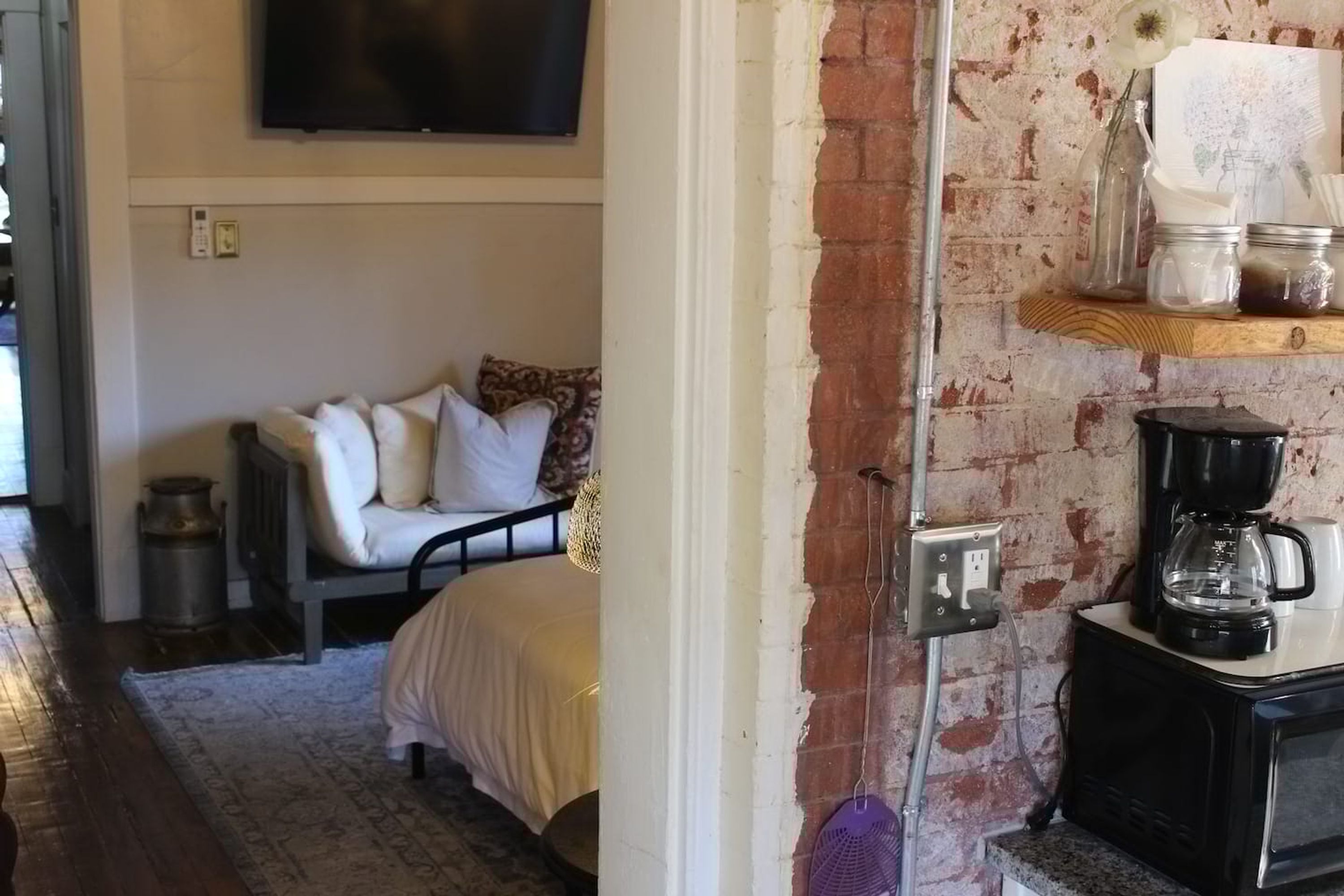 A cozy room with a bed, a coffee maker, and a shelf with jars.