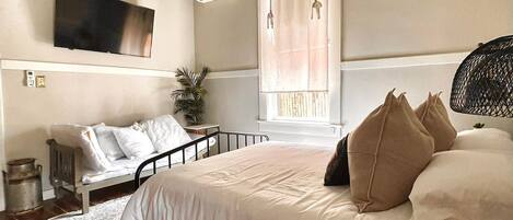 Une chambre à coucher comprenant un lit, un téléviseur fixé au mur, un appareil de climatisation et une fenêtre avec des rideaux.