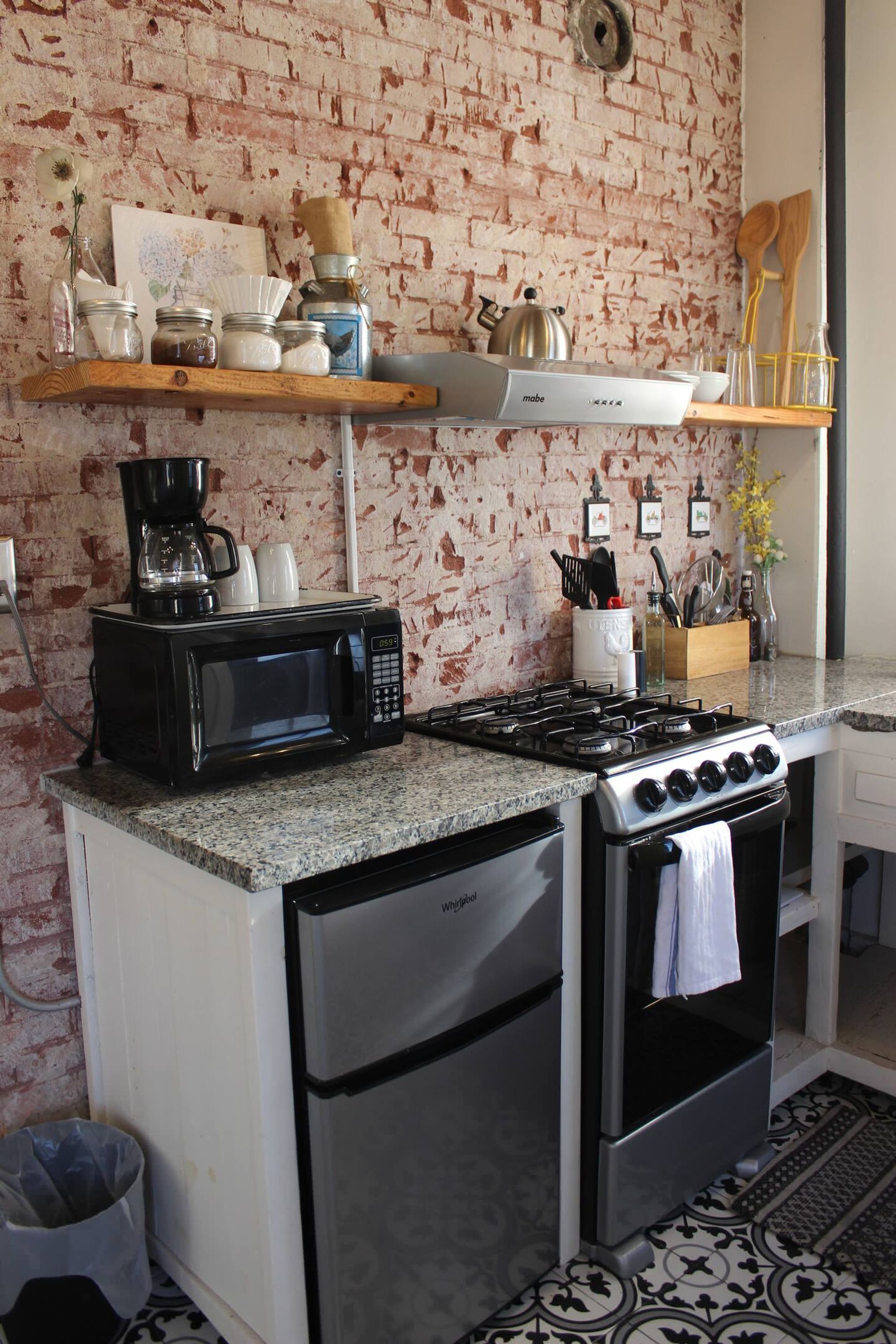 Een kleine keuken met een bakstenen muur, een magnetron, een fornuis en een koelkast.