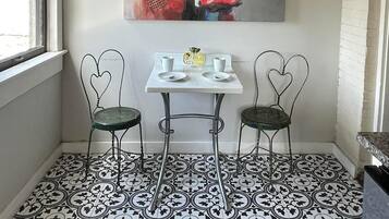 Un área de comedor con una mesa y dos sillas con forma de corazón, un cuadro de una vaca de colores en la pared, y un suelo con estampado.