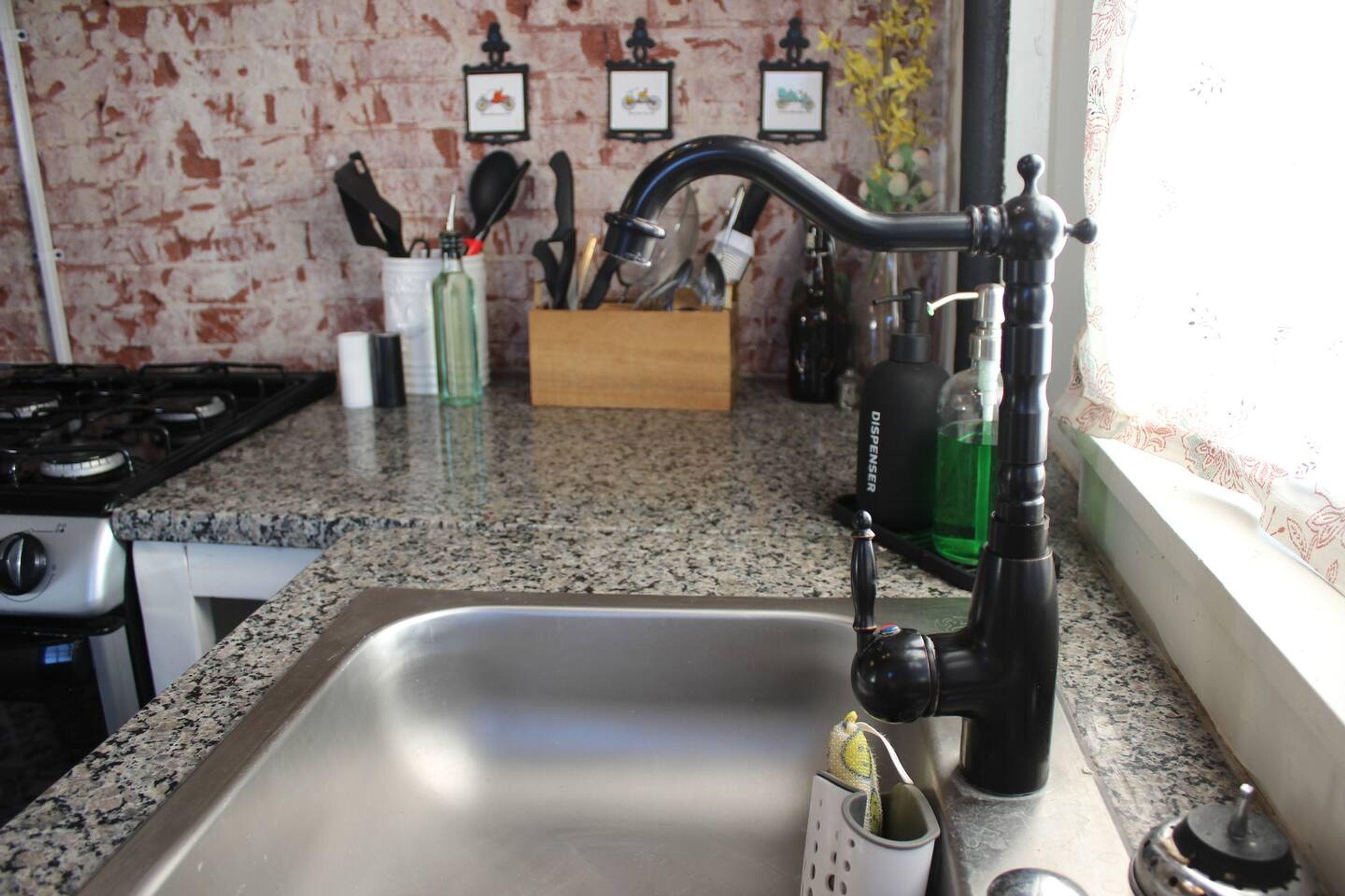 A kitchen with a stainless steel sink, a gas stove, and a wooden utensil holder.