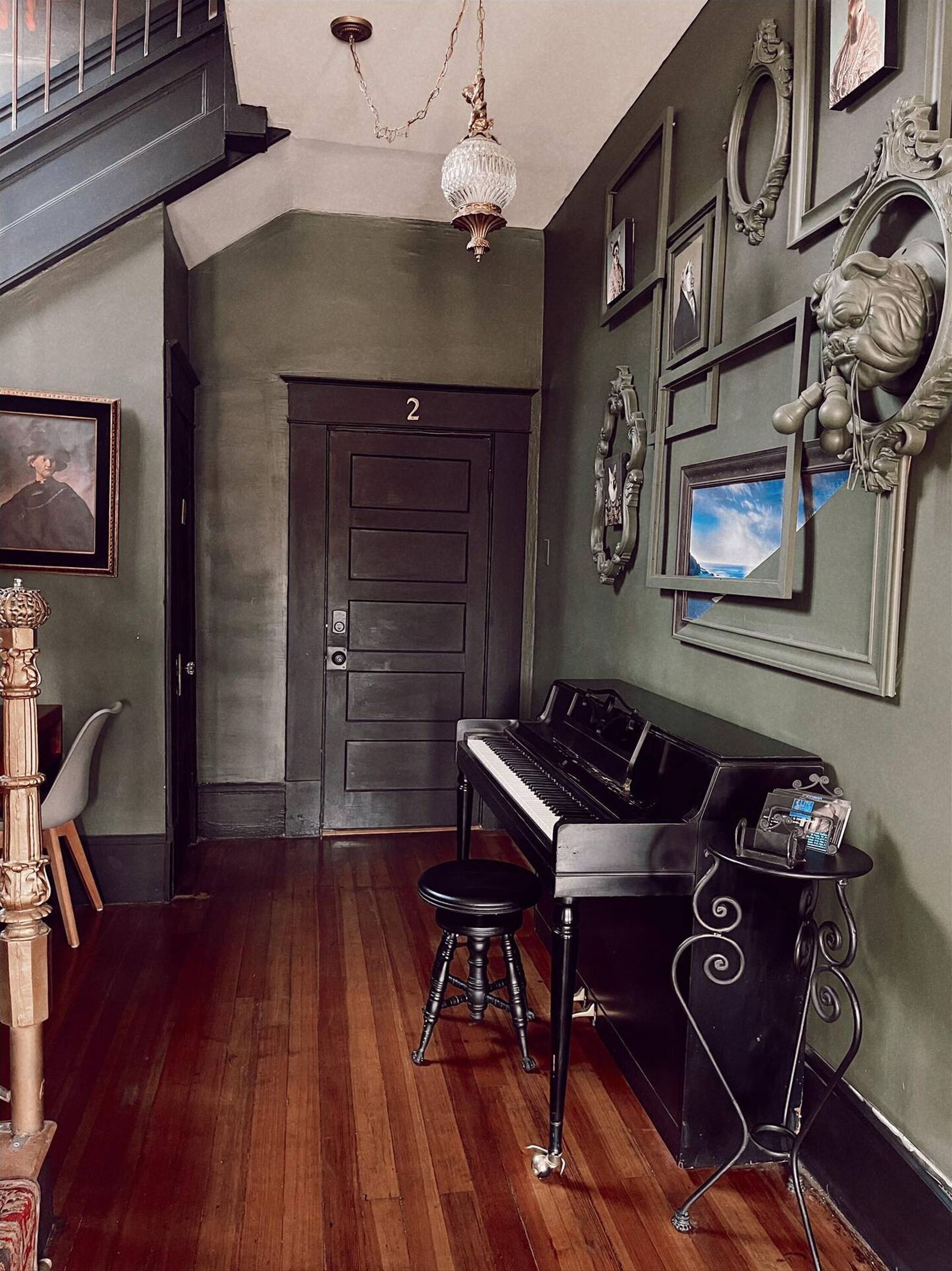 A room with a piano, a wooden chair, a door with the number 2, and a chandelier.