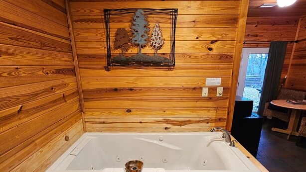 A wooden cabin interior with a large wooden bathtub, a framed picture of trees, and a small table with chairs. - Honey Bear Haven Suite 1 (Eureka Springs)