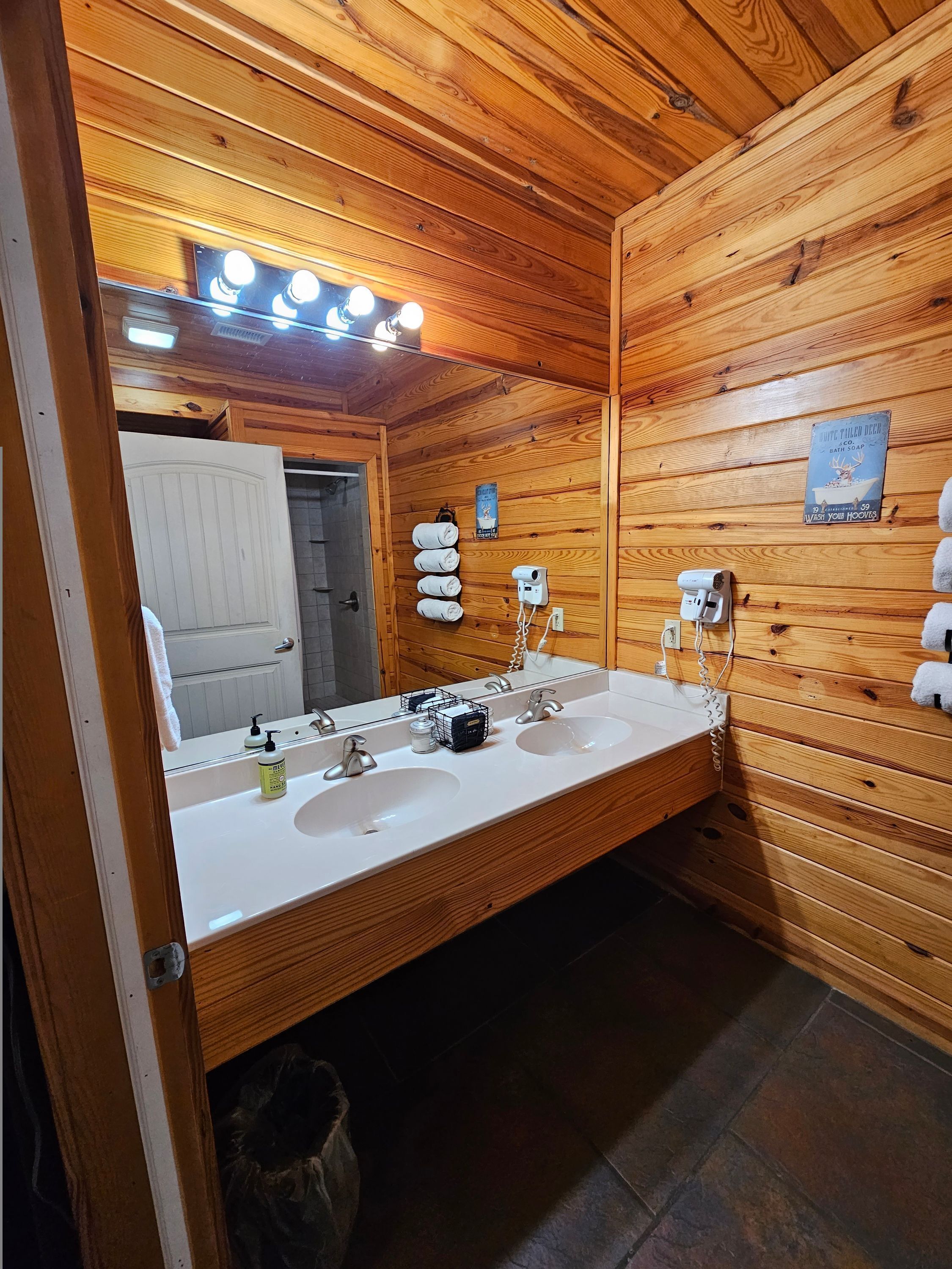 Un bagno in stile baita con specchio grande, due lavandini e un portasciugamani.