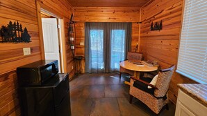 A wooden cabin interior with a dining area, kitchen, and a door leading outside. - Honey Bear Haven Suite 1 (Eureka Springs)