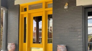 A modern building entrance with a yellow door, black brick walls, and two decorative pots. - Casa Mina 5 Central Rio Grande Historic Dist (El Paso)