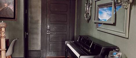 Una habitación con un piano, una silla de madera, una puerta con el número 2 y una araña.