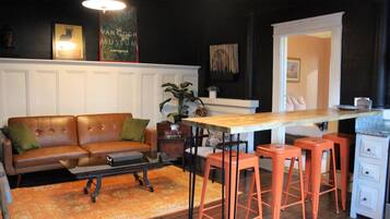 A living room with a brown leather sofa, orange stools, a wooden table, and a white cabinet.