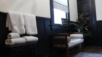 A room with a bench, a stack of towels, a potted plant, and a window with a sign.