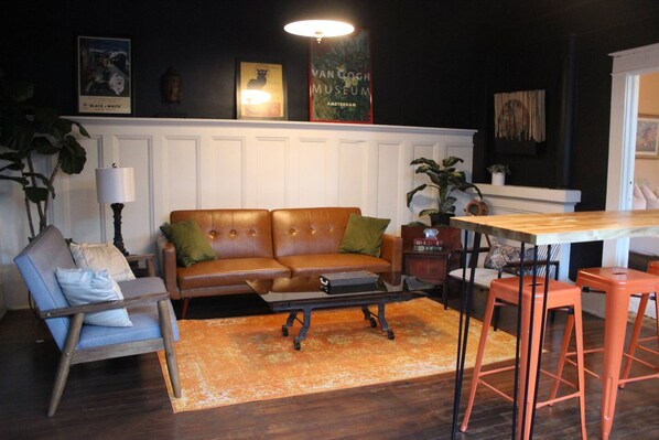 Un salon chaleureux avec un canapé en cuir marron, une table basse en bois et des tabourets de bar orange.