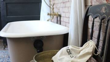 A vintage bathroom with a white sink, a brass faucet, and a wooden chair with a drawstring bag.