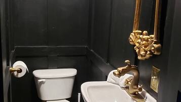 A small, dark-themed bathroom with a white toilet, a white sink, and a gold-framed mirror.