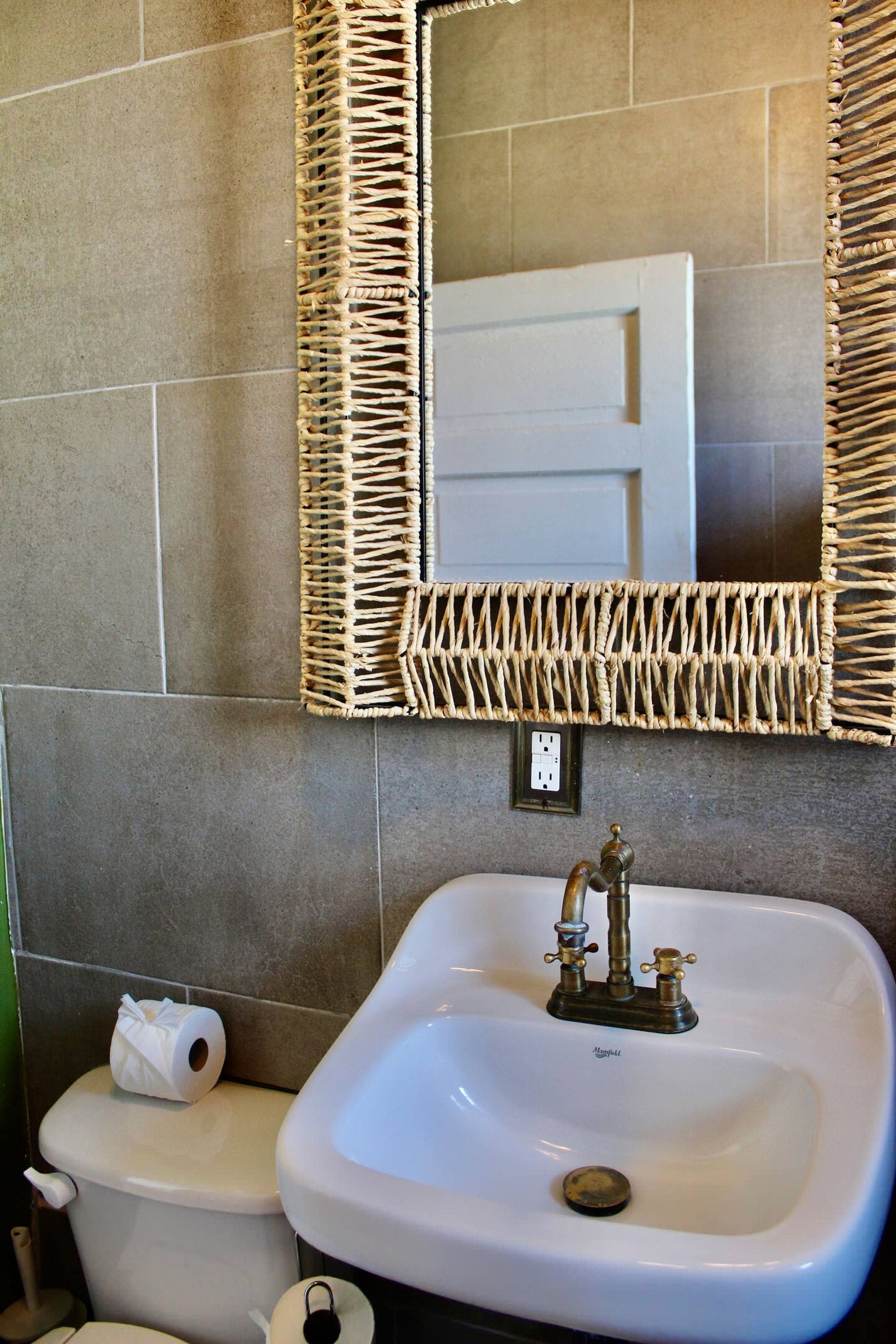 Een badkamer met een wit wastafel, een spiegel met een gevlochten omlijsting en een toilet.