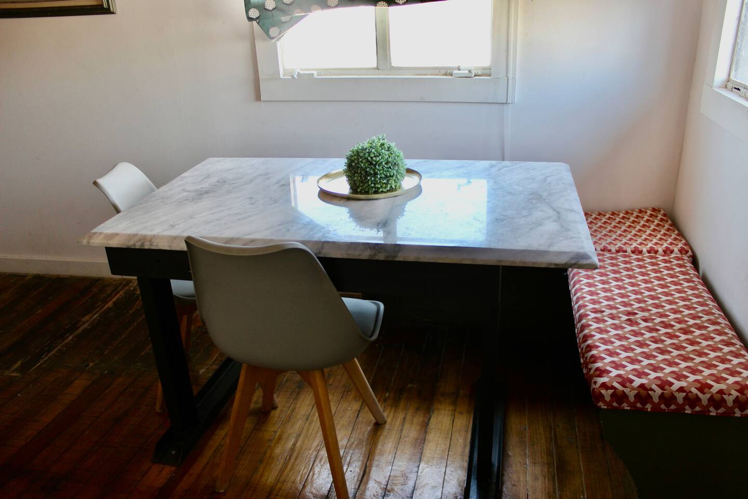 A dining area with a marble table, a potted plant, a gray chair, and a patterned bench.