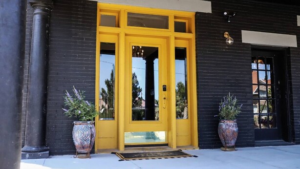 A building entrance with a yellow door, black brick walls, and two potted plants. - Casa Mina 4 Central Rio Grande Historic District (El Paso)