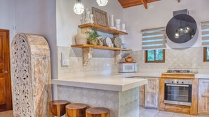 Uma cozinha com ilha central, banquetas de madeira, micro-ondas, fogão e prateleiras decorativas.
