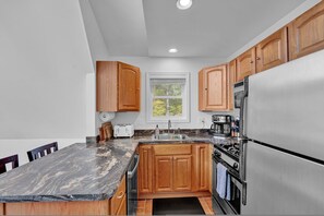 A modern kitchen with wooden cabinets, a granite countertop, stainless steel appliances, and a window providing natural light.
