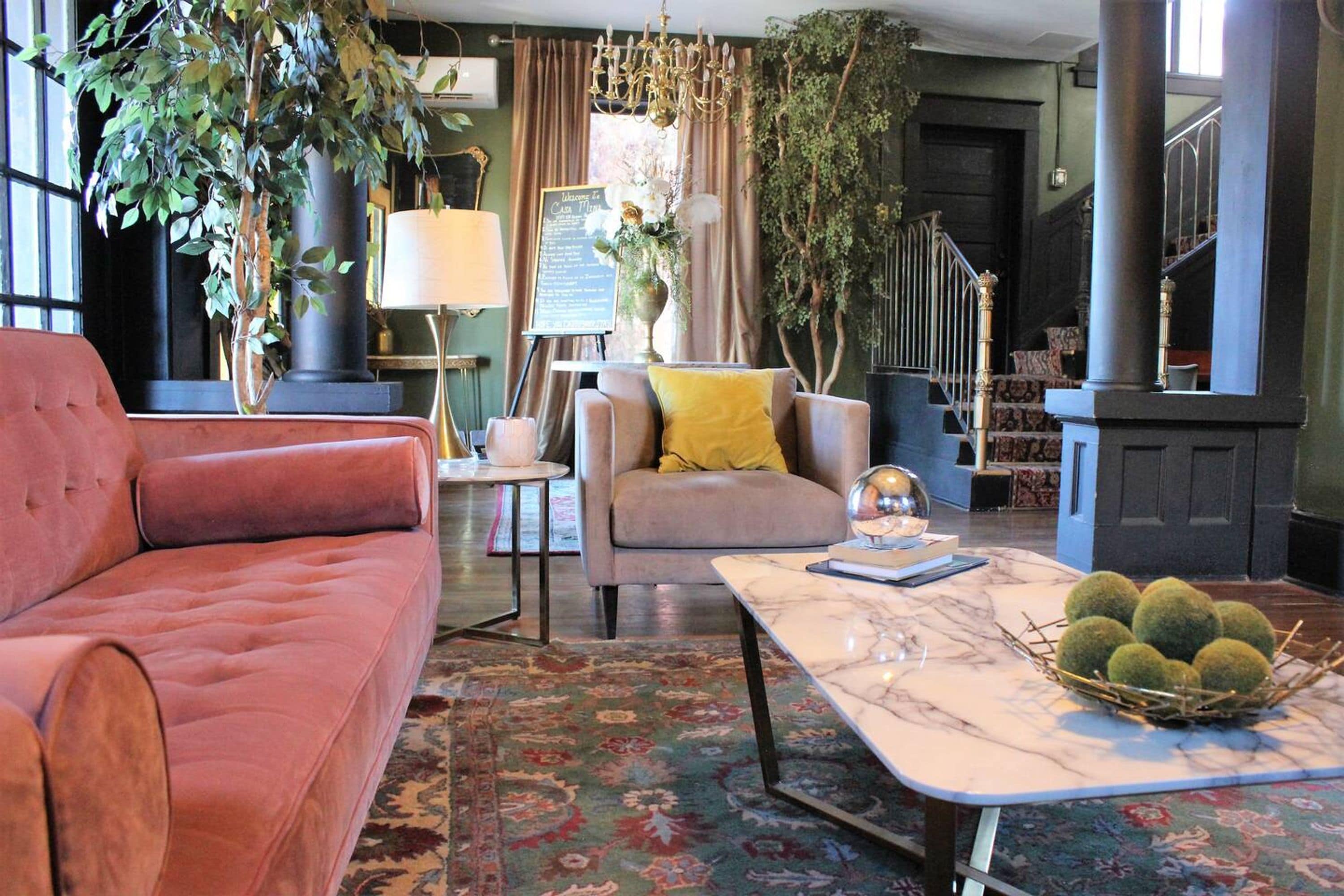 Un salón acogedor con un sofá rojo suave, un sillón gris con un cojín amarillo y una mesa de centro de mármol con un cuenco decorativo.