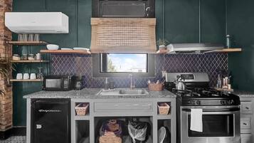 Una cucina con forno a microonde, fornello e forno integrati. Ci sono cesti sotto il bancone e un lavello con rubinetto.