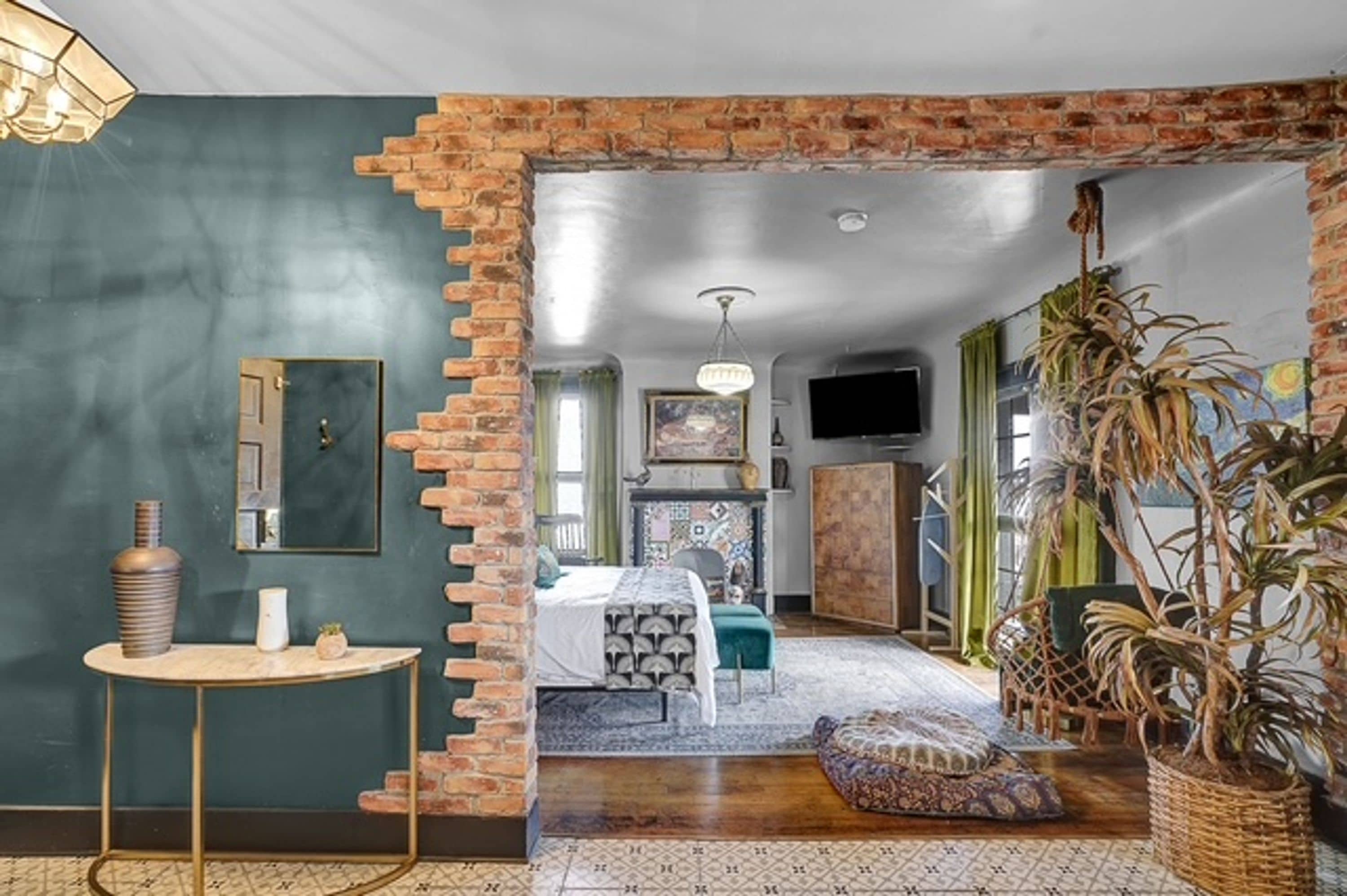 A room with a brick wall, a bed, a TV, and a plant.