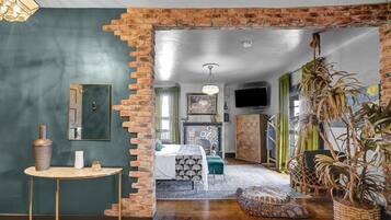 A room with a brick wall, a bed, a TV, and a plant.