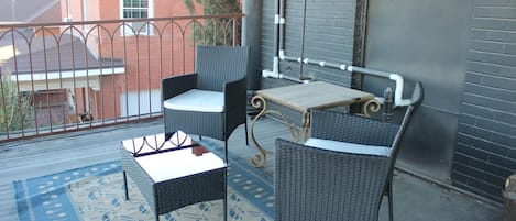 A balcony with wicker furniture, a table, and a patterned rug.