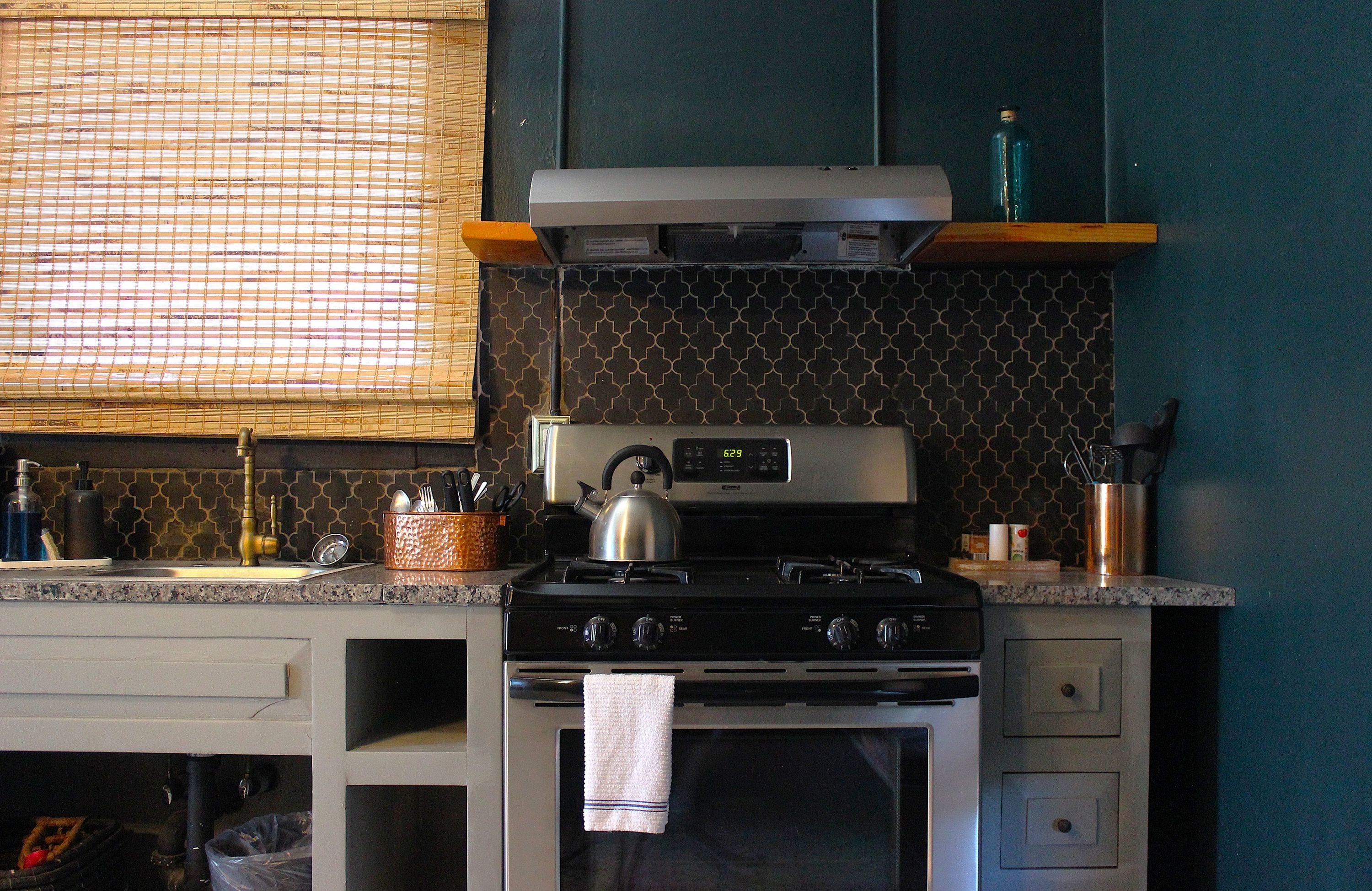 A kitchen with a stove, kettle, and various utensils.