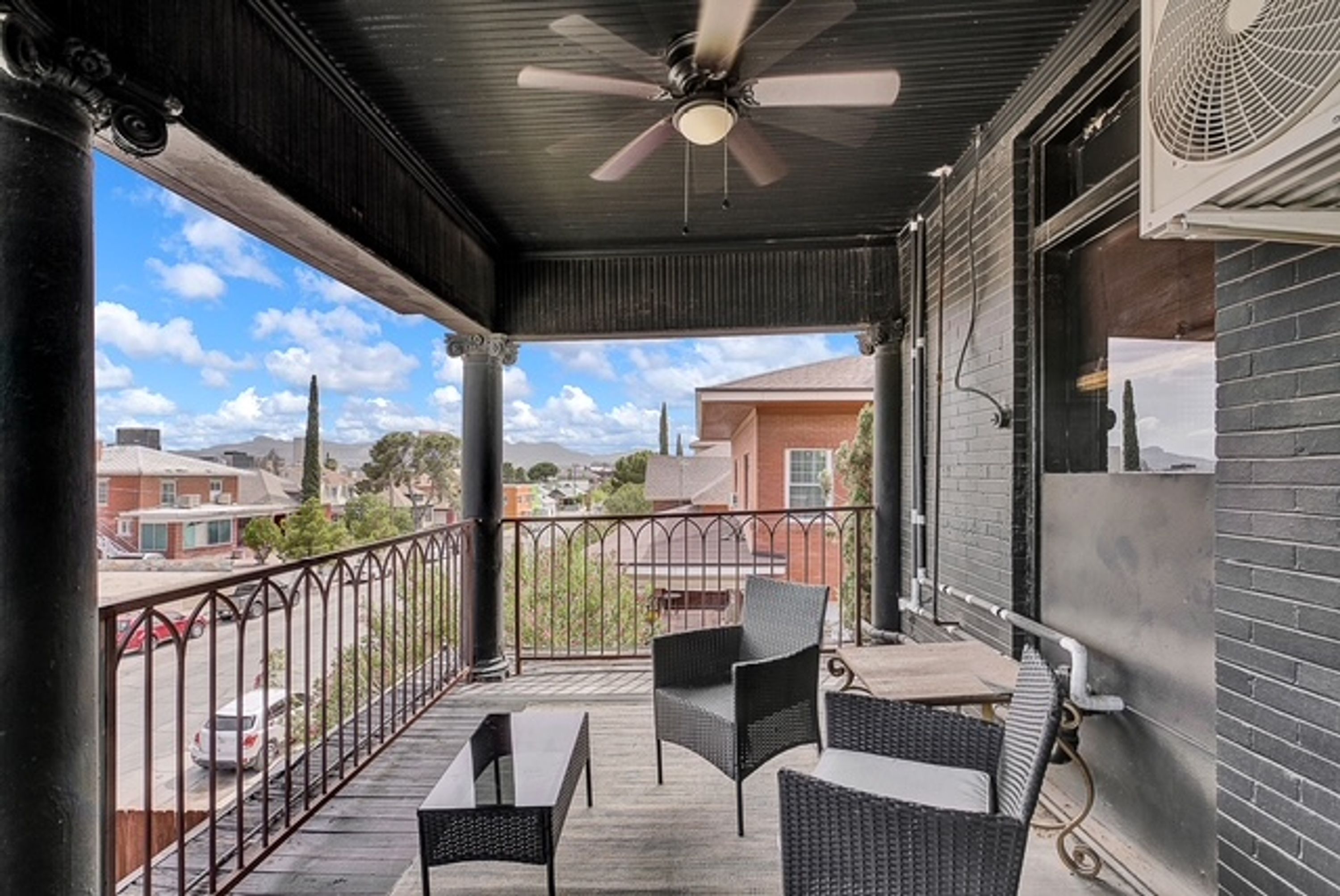 A covered outdoor area with a ceiling fan, two chairs, a table, and a view of the neighborhood.
