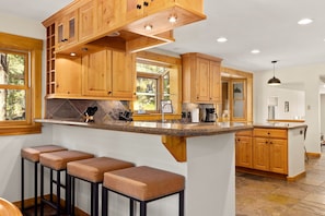 A kitchen with wooden cabinets, a granite countertop, and a bar area with stools. - Creekside Mountain Views Hot Tub (Evergreen)
