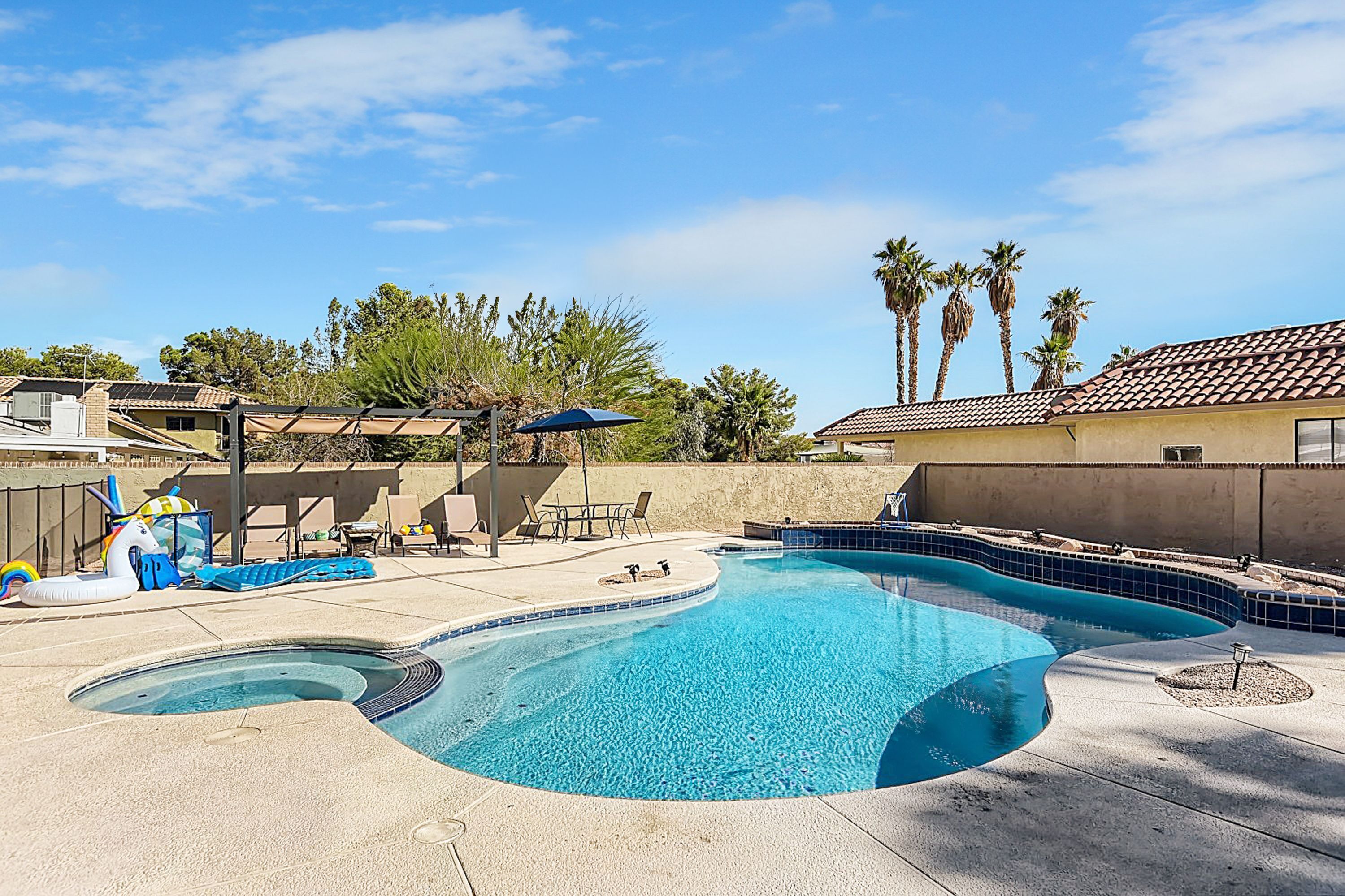 A swimming pool with a curved edge, surrounded by lounge chairs and umbrellas, with palm trees in the background.