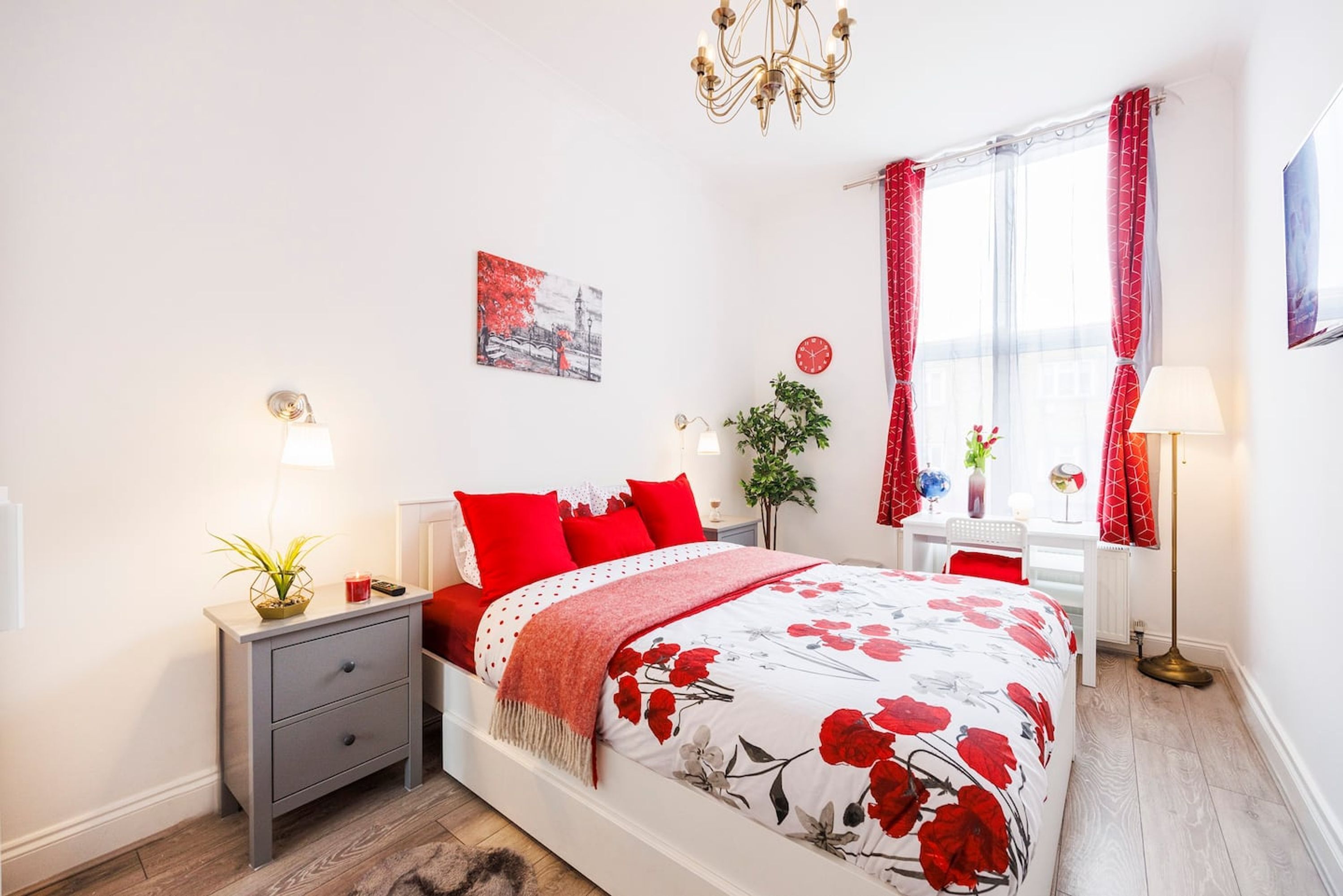 Un dormitorio con cama, mesitas de noche, una lámpara, una ventana con cortinas, una planta, un reloj y un cuadro en la pared.