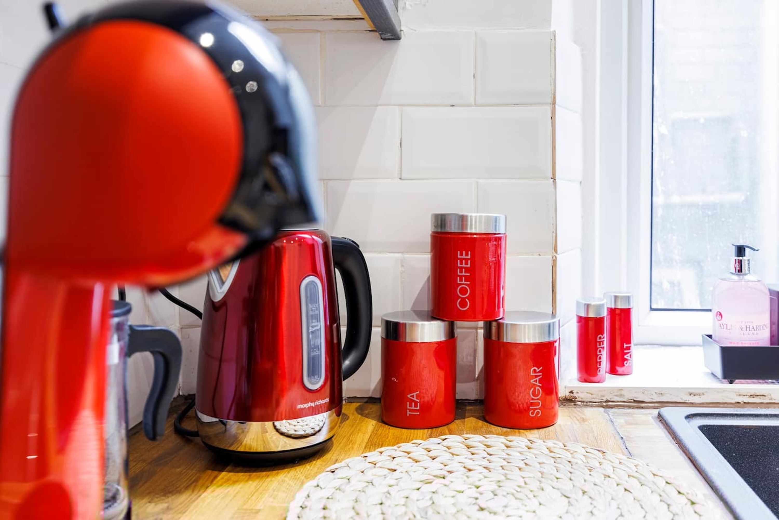 A kitchen with a red kettle, a coffee maker, and containers labeled 'tea', 'coffee', and 'sugar'.