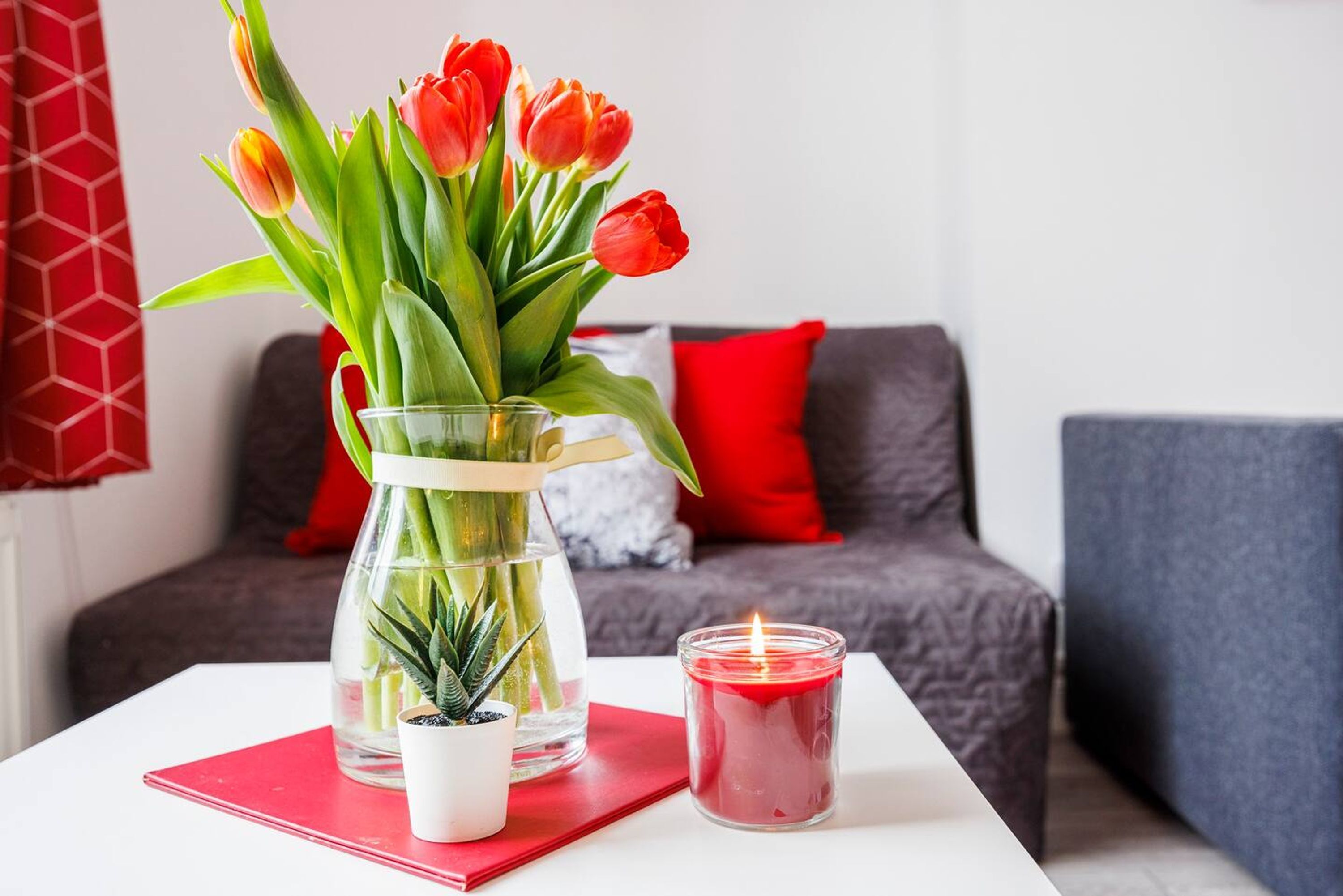 A table with a glass vase of red tulips, a lit candle, and a small potted plant.