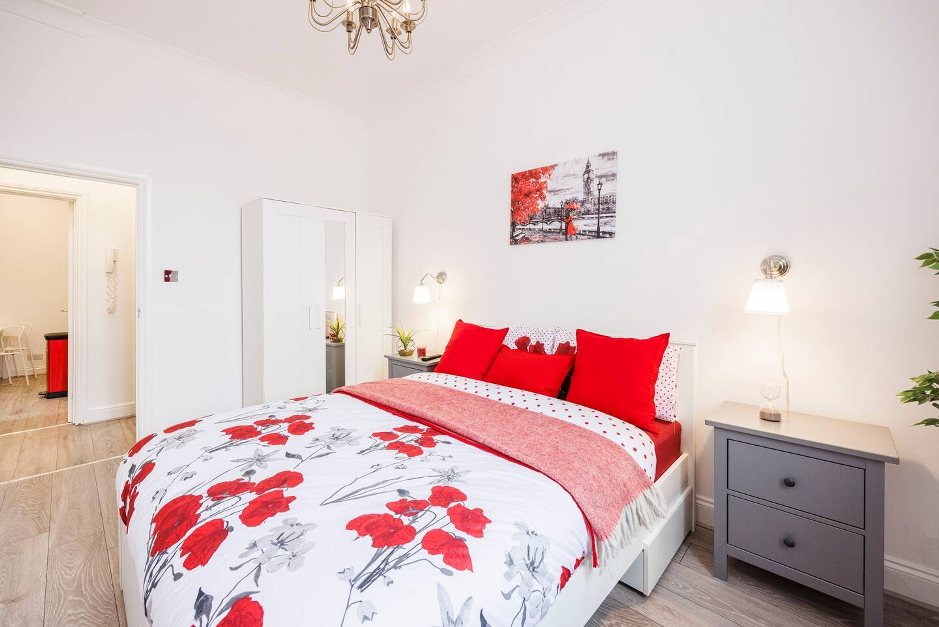 A bedroom with a bed, bedside tables, a nightstand, a painting, and a door.