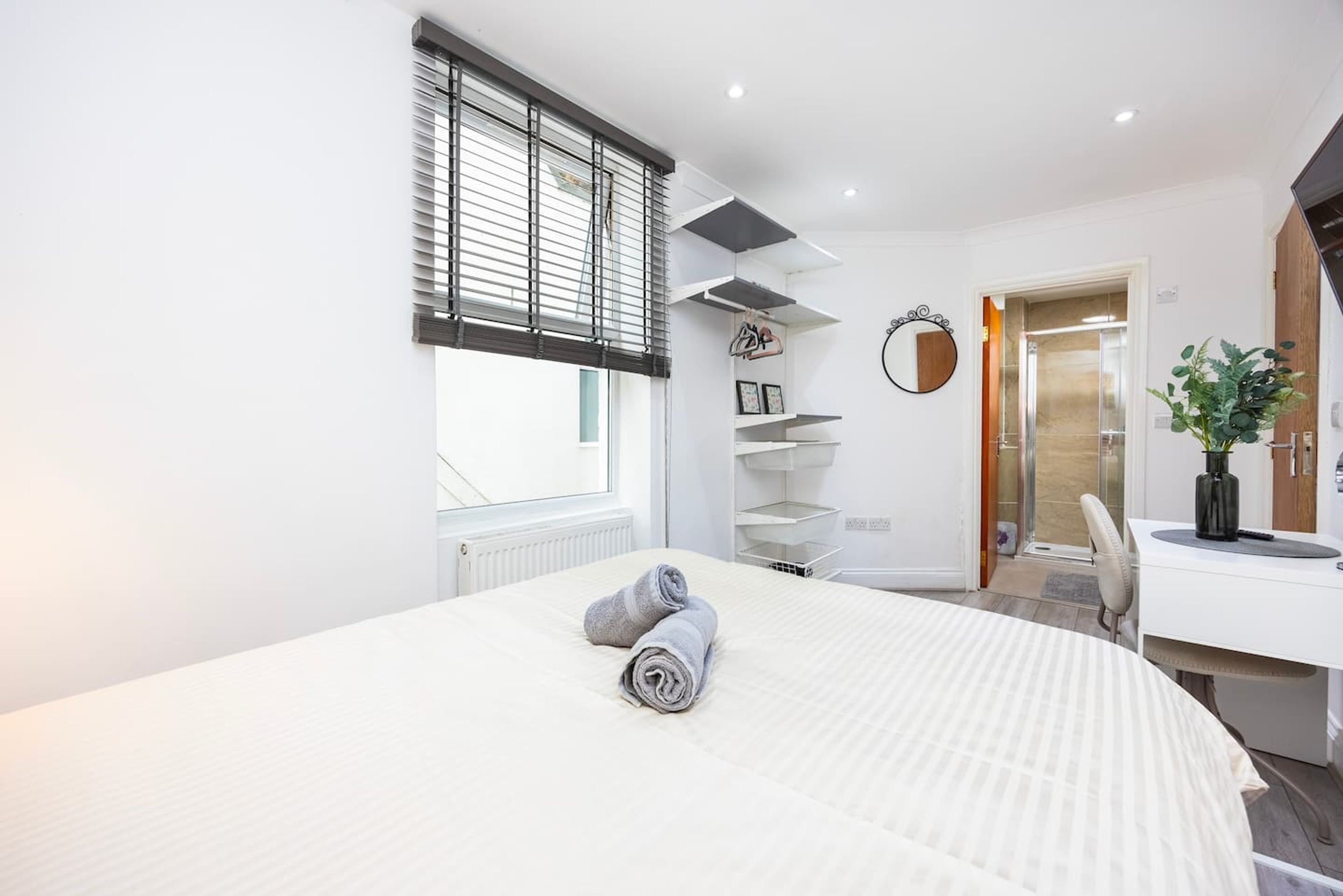 Un dormitorio moderno con una cama grande, una ventana con persianas, un escritorio con una silla y una planta en maceta.