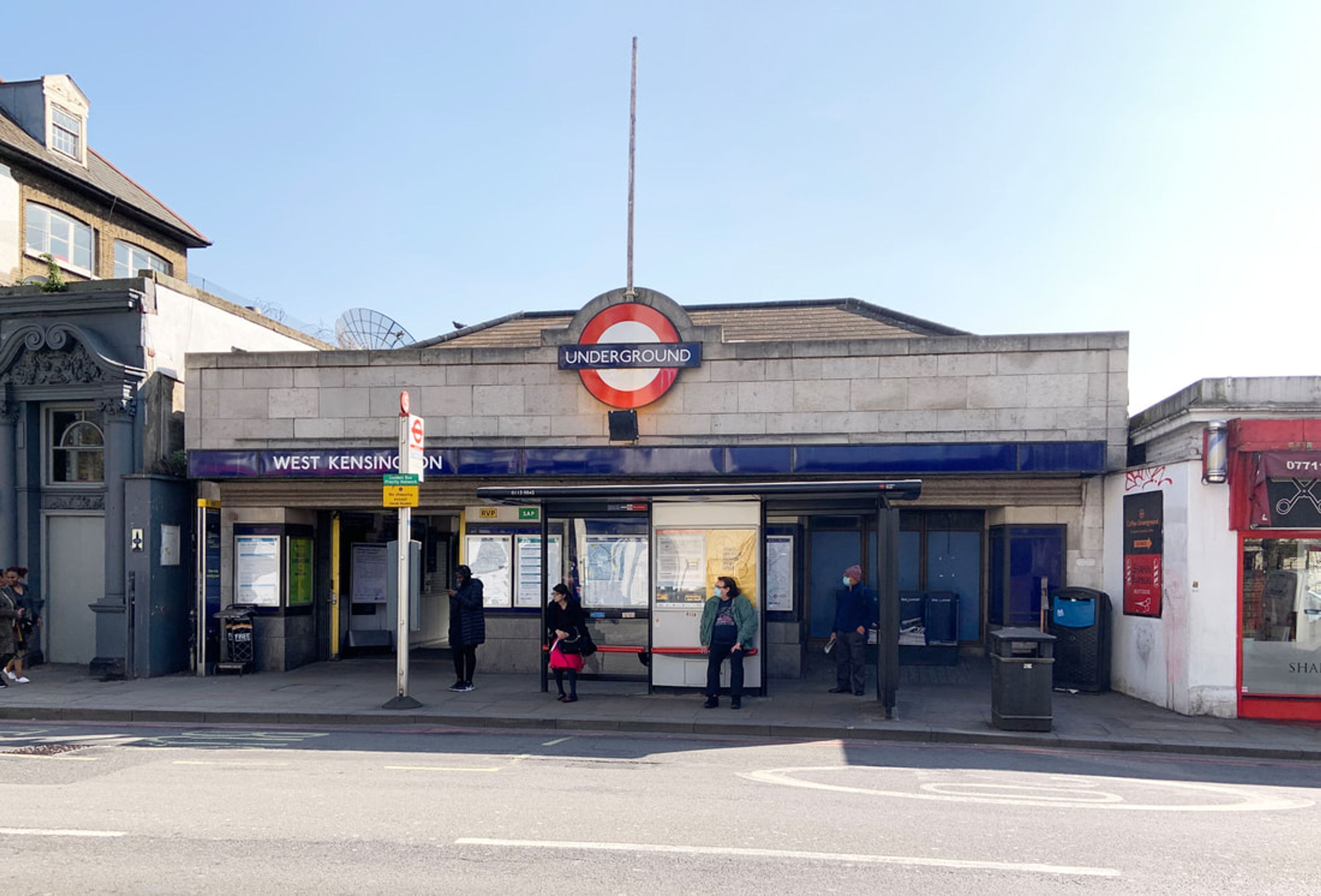 A bus stop with a sign for the Underground station, a shelter, and a bus.