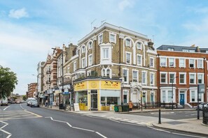 Vista de calle con una hilera de casas adosadas, un café llamado 'Crazy Coffee' y un letrero visible del 'NHS'.