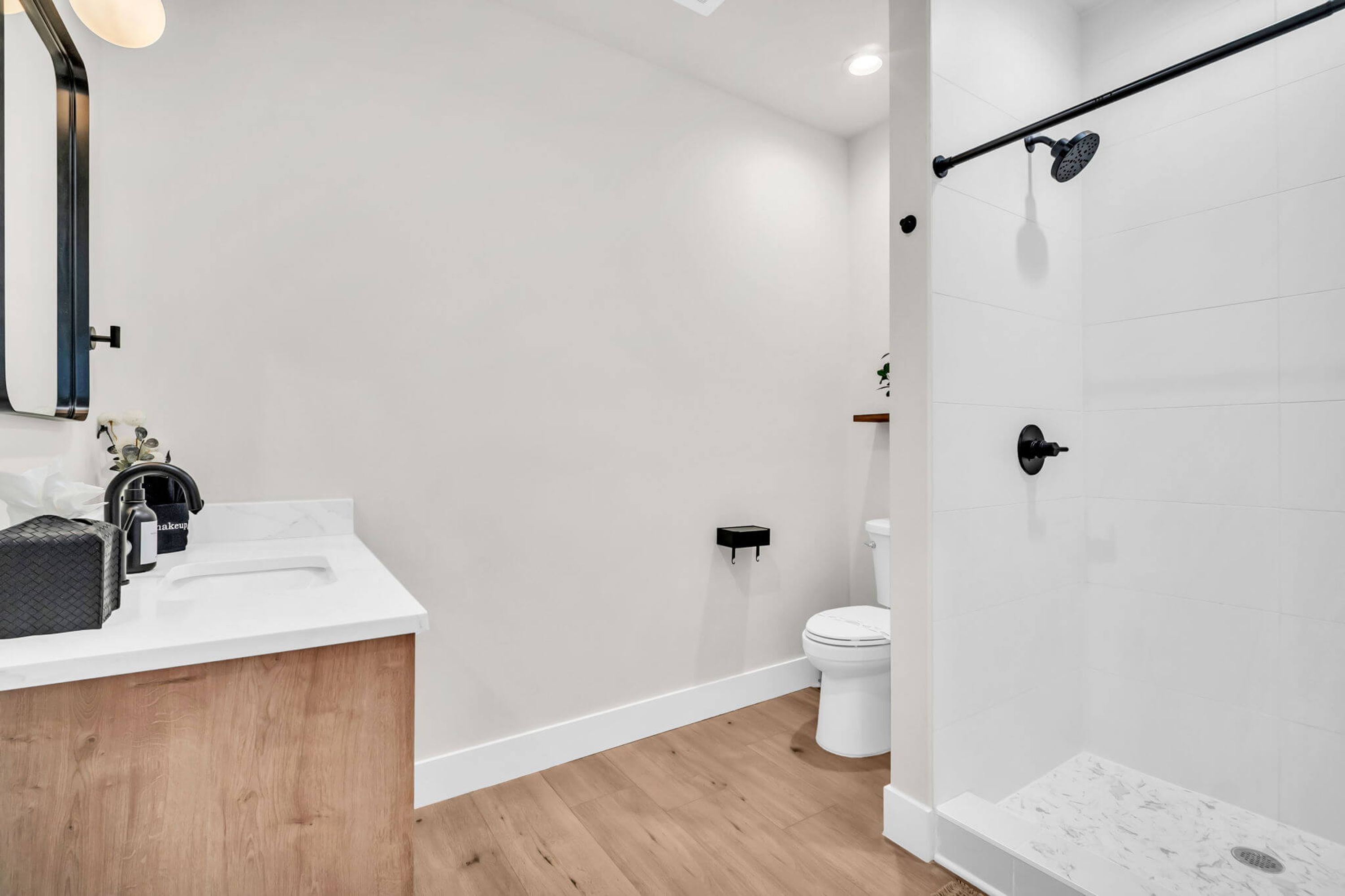 Un baño moderno con tocador de madera, un lavamanos blanco, un inodoro y una zona de ducha.