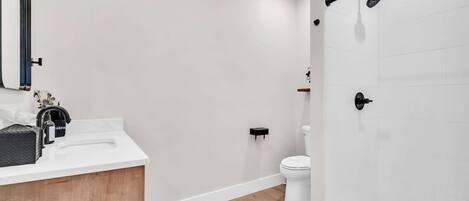 Un baño moderno con tocador de madera, un lavamanos blanco, un inodoro y una zona de ducha.