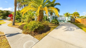 A residential area with a house, palm trees, and a sidewalk.