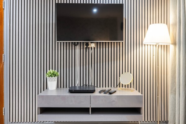 A modern living room with a flat-screen TV mounted on a wooden wall, a grey console table with a plant, remote controls, and a lamp. - 3 Bedroom Apartment by River Thames (London)