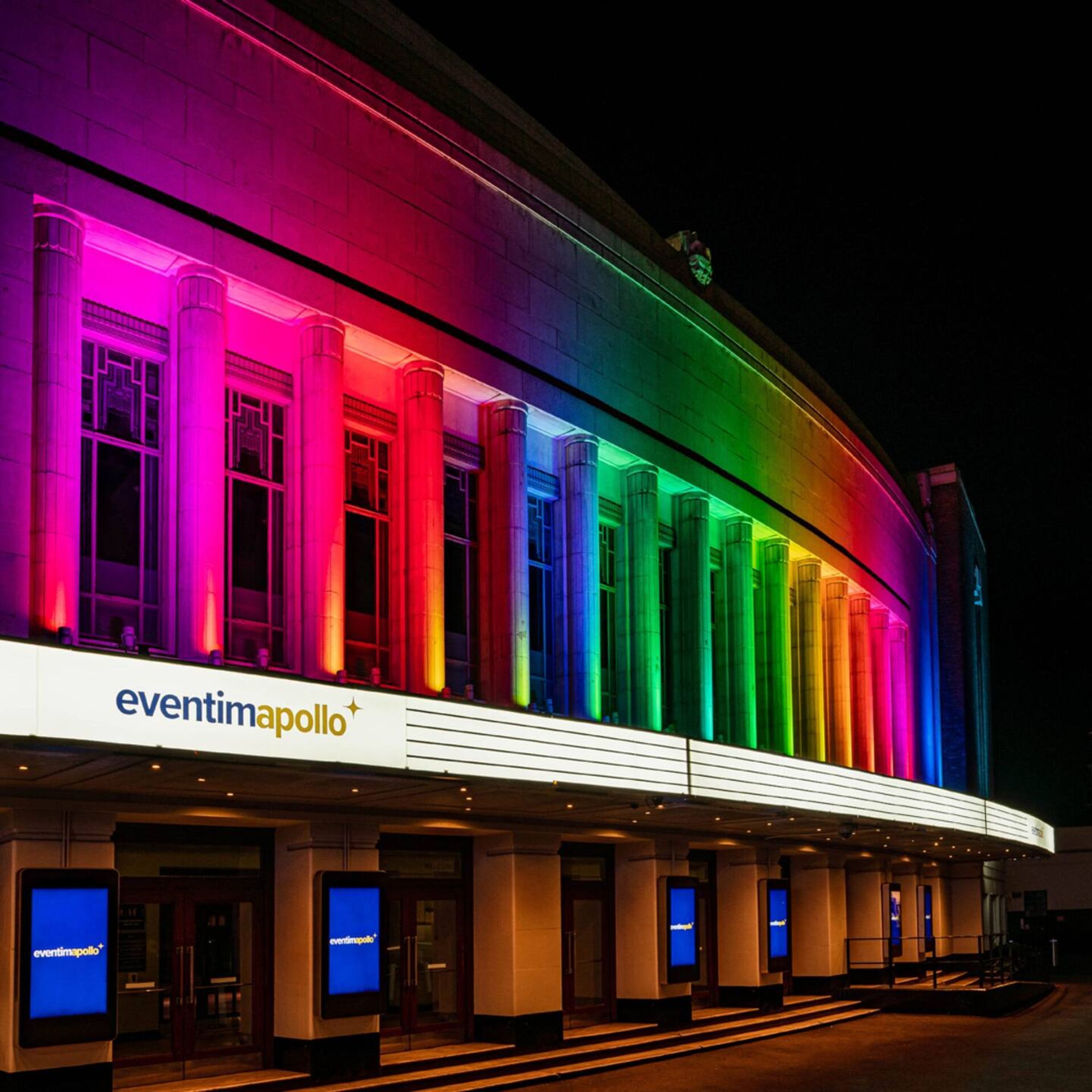 A building with a series of vertical columns illuminated in a spectrum of colors. The name "eventimapollo" is visible on the facade.