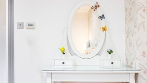 Ein weißes Schminktischchen mit rundem Spiegel, zwei kleinen Schubladen und zwei kleinen Topfpflanzen.