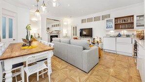 Una sala de estar moderna con una mesa de comedor de madera, sillas blancas, un sofá gris y un televisor.